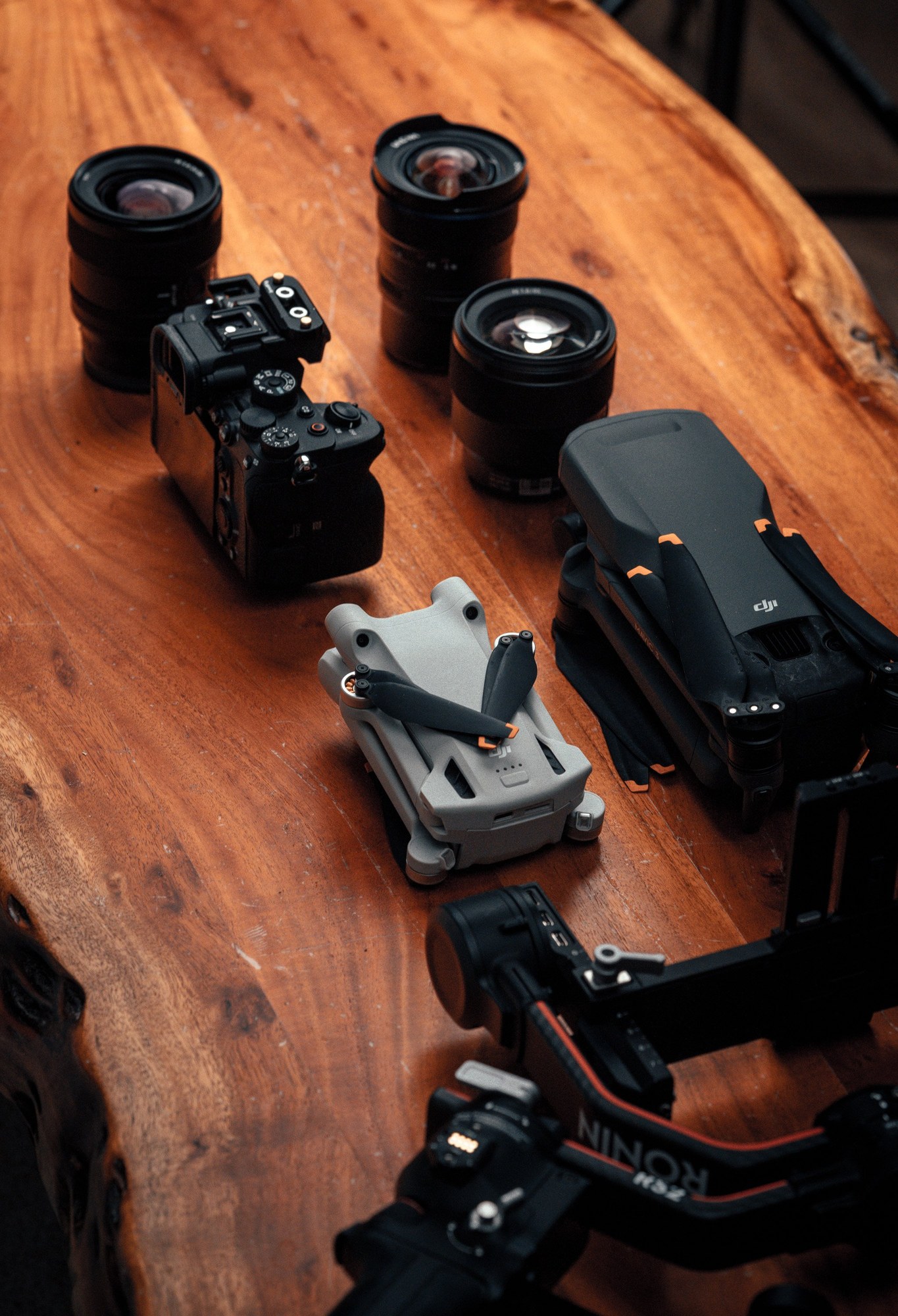Camera bodies, lenses, a drone and its controller laid out on a wooden table.