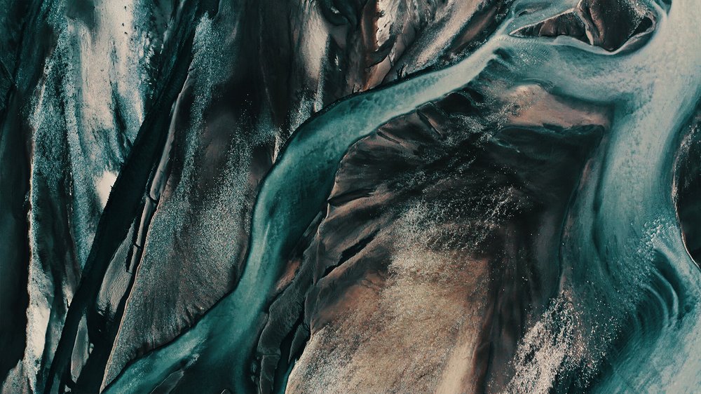 Close-up aerial view of winding blue-green river flowing through arid terrain with brown and sandy areas.