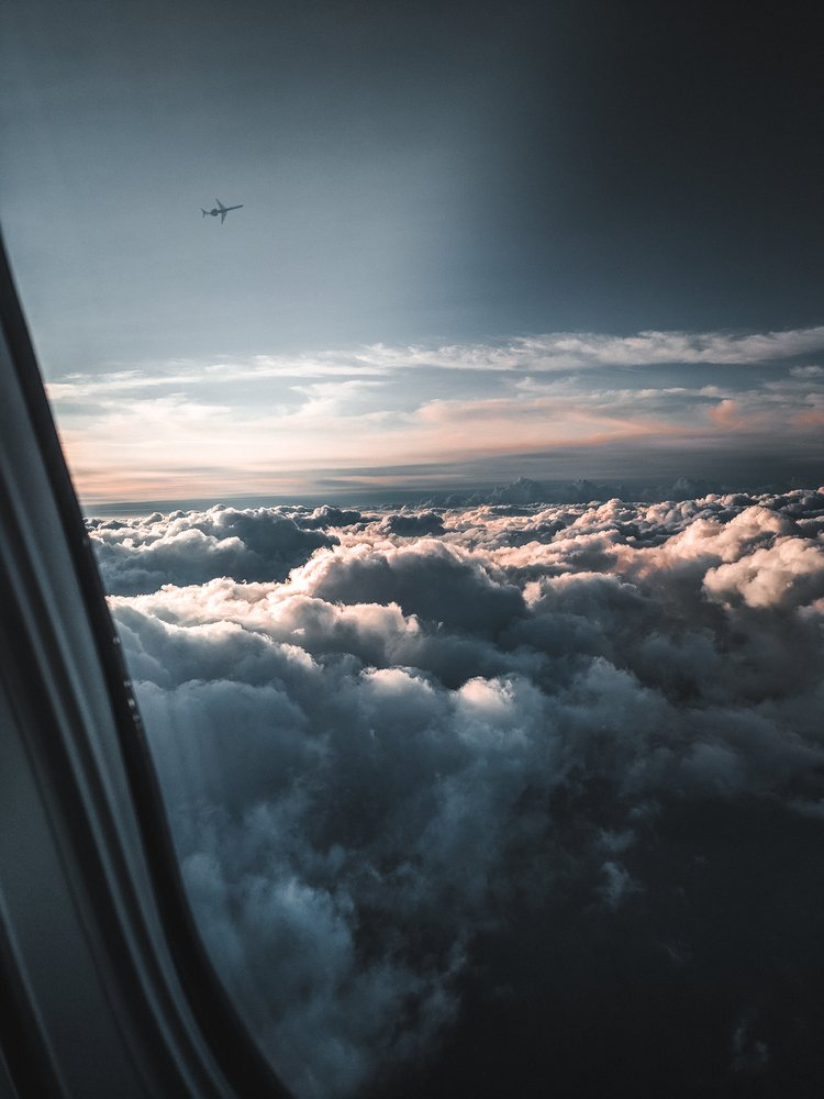 View from an airplane window showing clouds and an airplane flying in the sky during sunset.