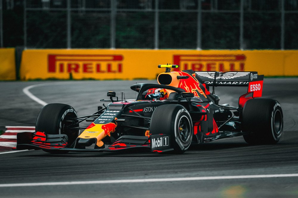 A Formula 1 race car on a racetrack, featuring Red Bull Racing livery with branding such as Aston Martin, Pirelli, and Mobil. The background includes a Pirelli advertisement and a chain-link fence.