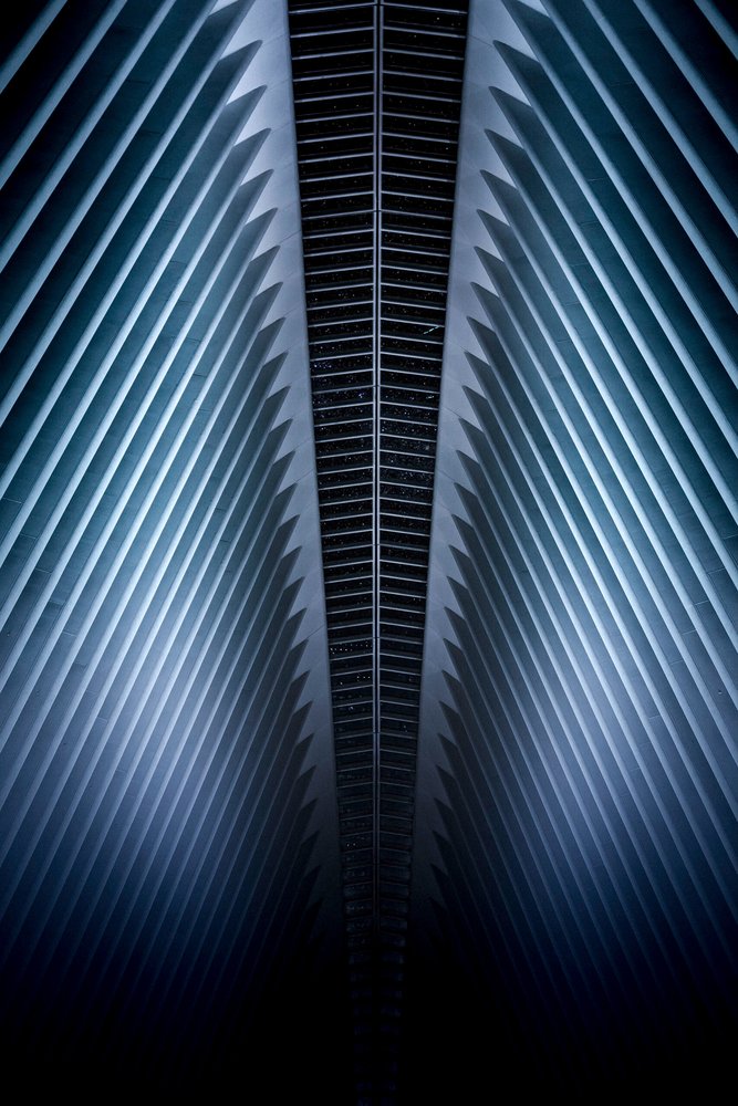 A modern building with symmetrical metallic ribbed architecture and dark windows, viewed from below.