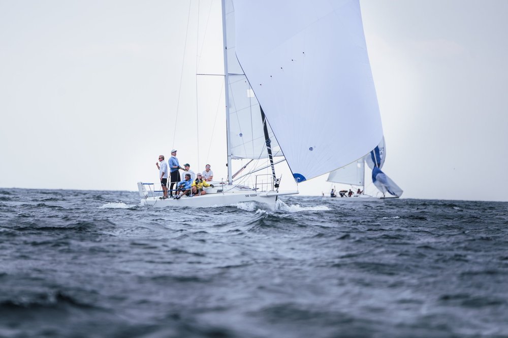 A group of people sailing on a white sailboat with a large white sail on a body of water in daytime.