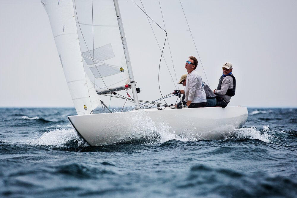 Four people sailing on a small white sailboat in open water.